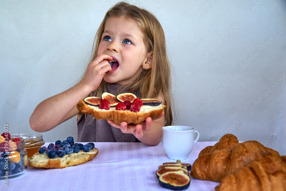 Blonde girl on a white background with a croissant and a cup of milk. Happy child's healthy breakfast. High quality photo Blonde girl on a white background with a croissant and a cup of milk. Happy child's healthy breakfast. High quality photo
