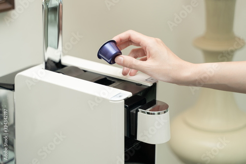 Close up of woman hand pressing button on a capsule into a coffee machine.