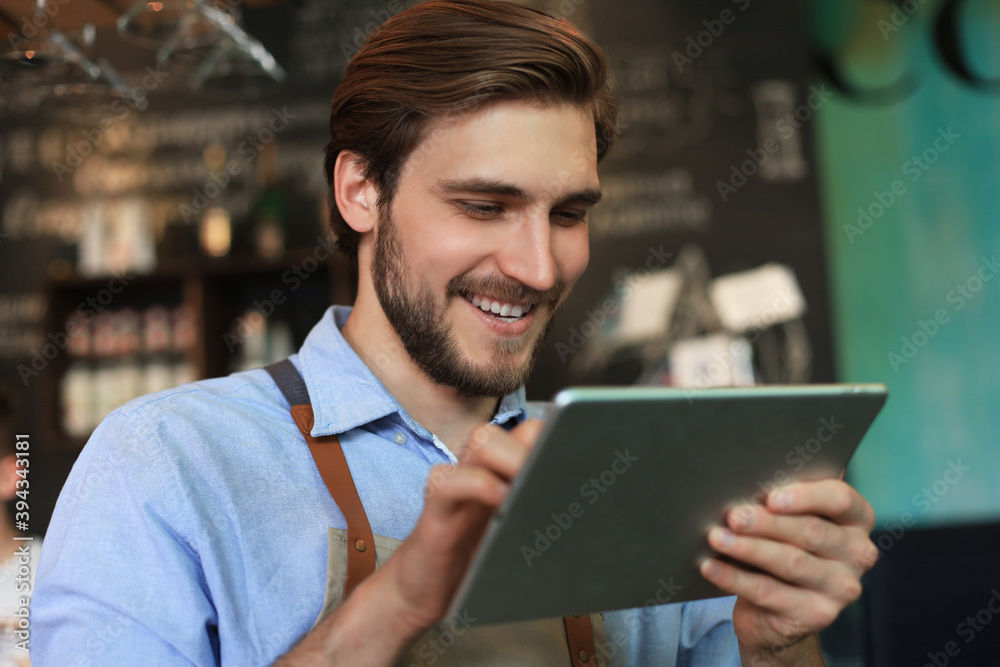 Young male owner using digital tablet while standing in cafe. Young male owner using digital tablet while standing in cafe.