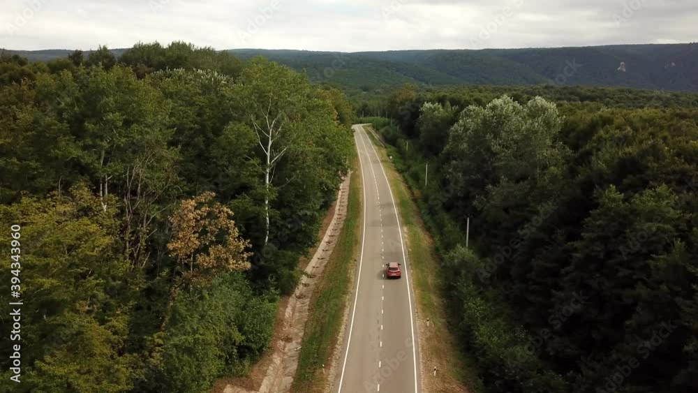 Orange SUV car driving on a rural road in the mountains and forest at summer sunny day - Drone point track view. Orange SUV car driving on a rural road in the mountains and forest at summer sunny day - Drone point track view.