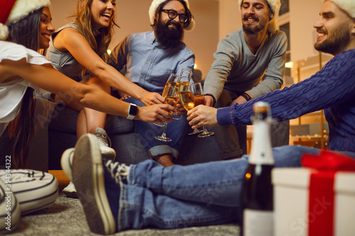 Group of friends sitting on floor and clinking glasses of champagne during Christmas holiday festive party
