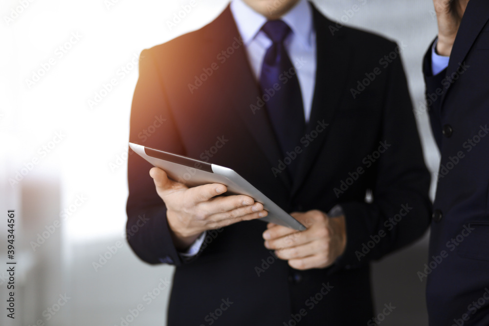 Business people use a tablet computer for discussion of their new project, standing in sunny modern office. Unknown businessman or male entrepreneur with a colleague at workplace Business people use a tablet computer for discussion of their new project, standing in sunny modern office. Unknown businessman or male entrepreneur with a colleague at workplace