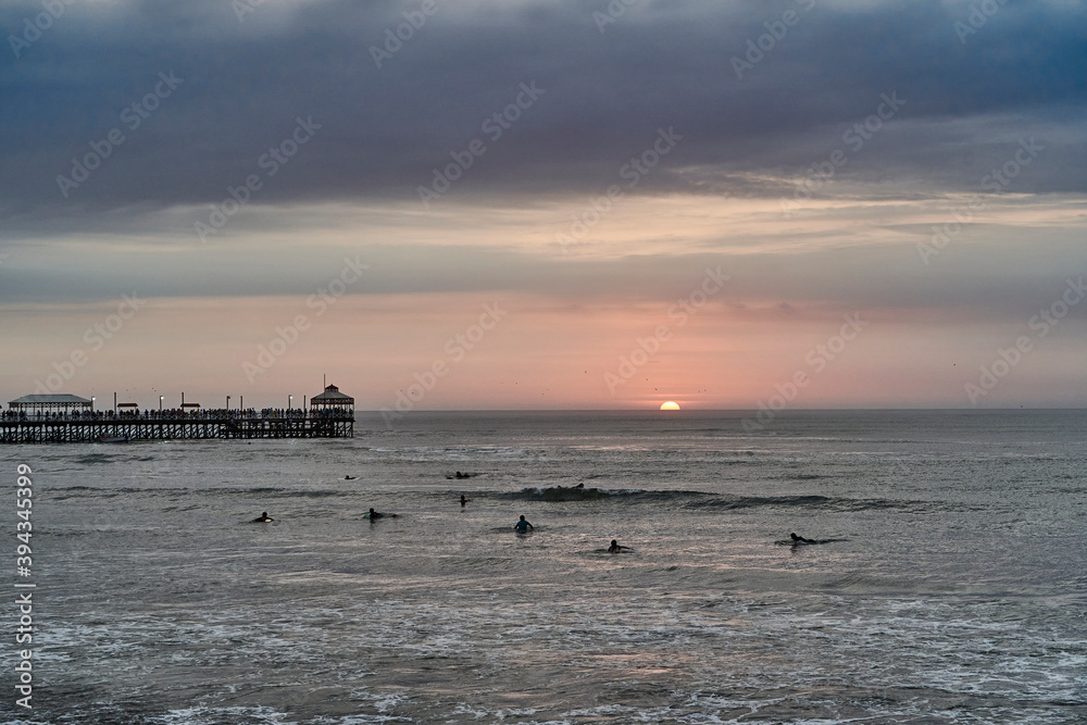 Playa Varadero, Huanchaco, at sunset over the pacific ocean with some surfers in the water and the long jetty in the background