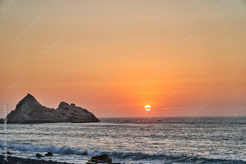romantic sun set over the pacific ocean at a beach on the coast of Peru with dramatic sky during the golden hour, with guano covered rock in the background