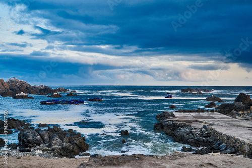 fishing boats lying in the surf at the coastline of Peru, a place were desert meets the ocean. Showing blue sky, dramatic clouds and fishing huts and boats