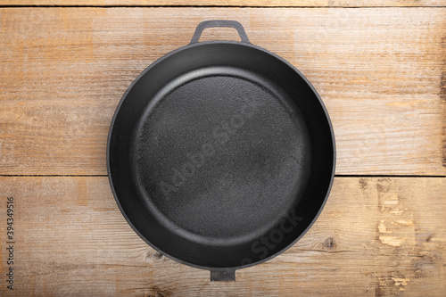 Empty cast iron pan on wooden culinary background, space for text.