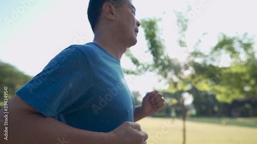 Mid adult Asian man running along the running track at the park on a sunny day in slow motion. Retirement Health care motivation, fight cancer building strong immune system, side view camera