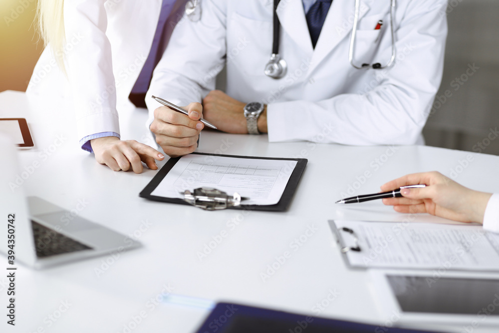 Group of unknown doctors are sitting at the desk and discussing problems or disease treatment in sunny hospital office. Covid 2019 Group of unknown doctors are sitting at the desk and discussing problems or disease treatment in sunny hospital office. Covid 2019