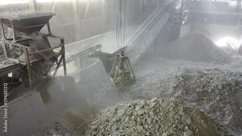 production workshop, crushing stones, huge bucket pick up stone blocks and lifts  into powerful unit. fractions and sorting on carpet line. rays of sun through dusty workshop, chemical industry grind