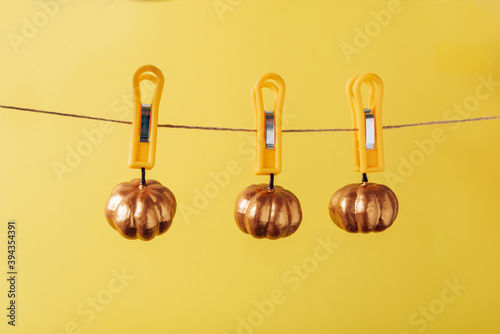Small pumpkin hanging on clothespins on a yellow background