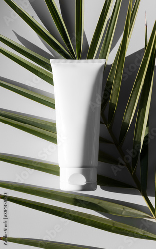 Top view of a white tube of cream mockup with a palm leaf.