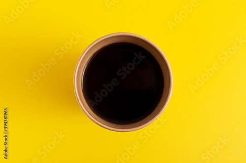 Black coffee in disposable paper cup on yellow background. Top view.