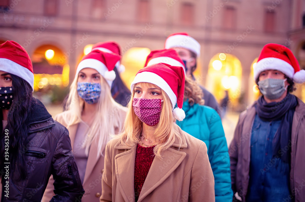Friends group walking at city wearing face mask and santa hat in coronavirus time - New normal walk concept with young people covered by protective mask in Christmas holiday Friends group walking at city wearing face mask and santa hat in coronavirus time - New normal walk concept with young people covered by protective mask in Christmas holiday