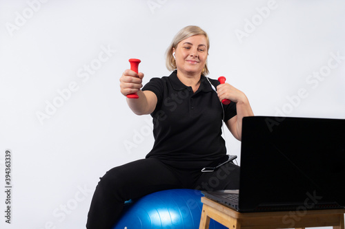 Senior woman doing fitness exercise online, on a itness sword holding dumbbells. photo