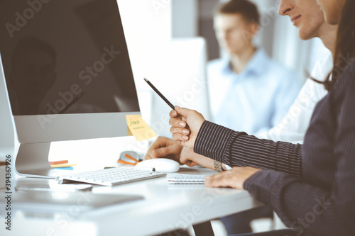 Business woman and man are discussing questions while using computer and blocknote in modern office, close-up. Teamwork in business photo