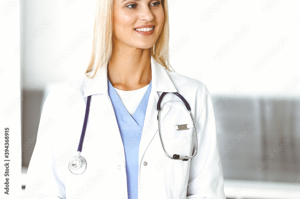 Fototapeta premium Woman-doctor at work in hospital is happy to communicate with female patient. Blonde physician checks medical history record and exam results. Medicine concept