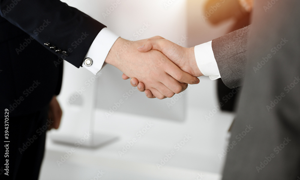 Unknown businessman shaking hands with his colleague or partner while standing straight in sunny office, close-up Unknown businessman shaking hands with his colleague or partner while standing straight in sunny office, close-up