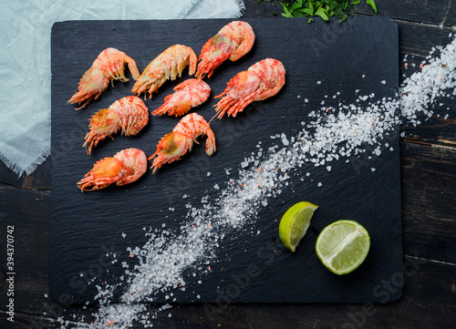 Tiger shrimps with lime, salt crystals on black slate board. Top view