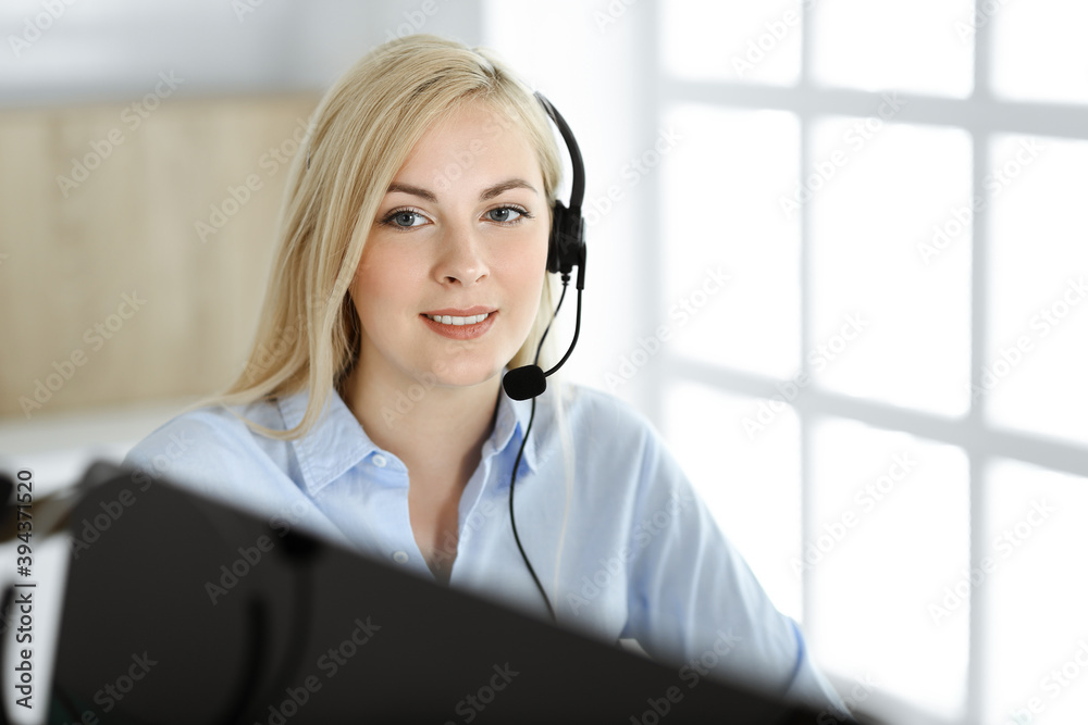 Blonde business woman sitting and communicated by headset in call center office. Concept of telesales business or home office occupation Blonde business woman sitting and communicated by headset in call center office. Concept of telesales business or home office occupation