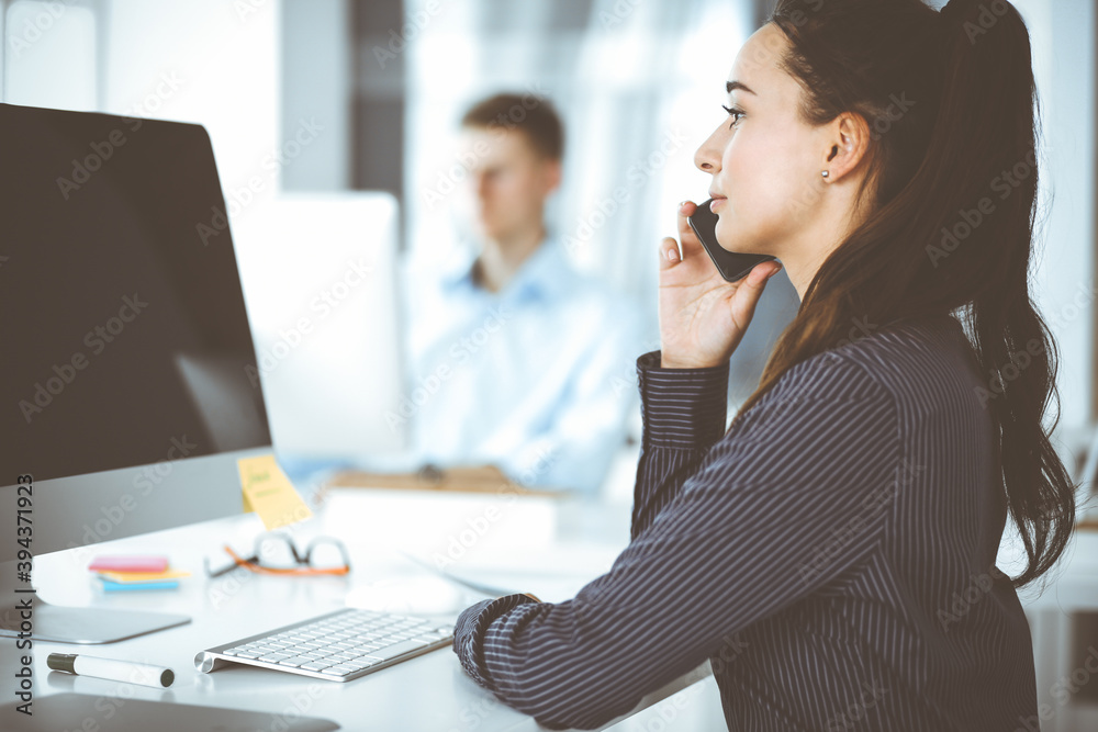 Business woman using computer at workplace in modern office. Brunette secretary or female lawyer smiling and looks happy. Working for pleasure and success Business woman using computer at workplace in modern office. Brunette secretary or female lawyer smiling and looks happy. Working for pleasure and success