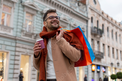 A smiling man with a coffee cup is walking and holding shopping bags.