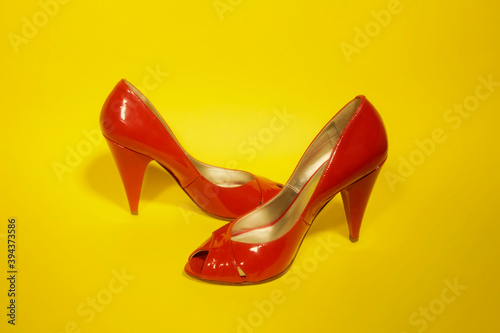 A pair of shiny sexy red shoes, over a yellow background. Party, leisure time, elegance. 