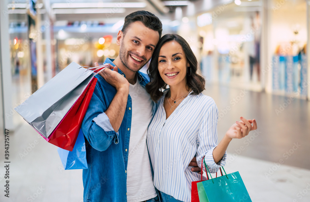 Beautiful happy excited couple in love or family with paper bags in hands while walking during shopping in the mall Beautiful happy excited couple in love or family with paper bags in hands while walking during shopping in the mall