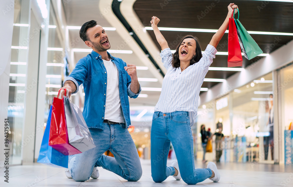Fototapeta premium Excited winning couple in love or family with paper bags in hands while are shouting during shopping in the mall