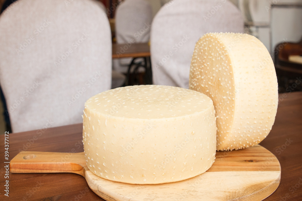 round parmesan or pecorino cheese on a wooden board. Two heads of cheese. Background.