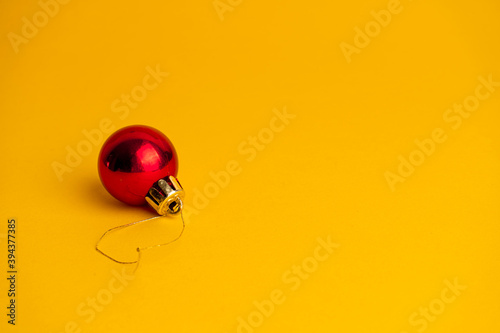 Red ball decoration of a Christmas tree on a yellow background. Copy space © Kate