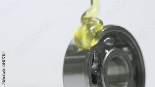 Closed up macro, Pouring yellow oil into ball bearing isolated on white backgroud with copy space. Oil help to protect wear and rust. Reduce friction. Engineering, service and industrial concept