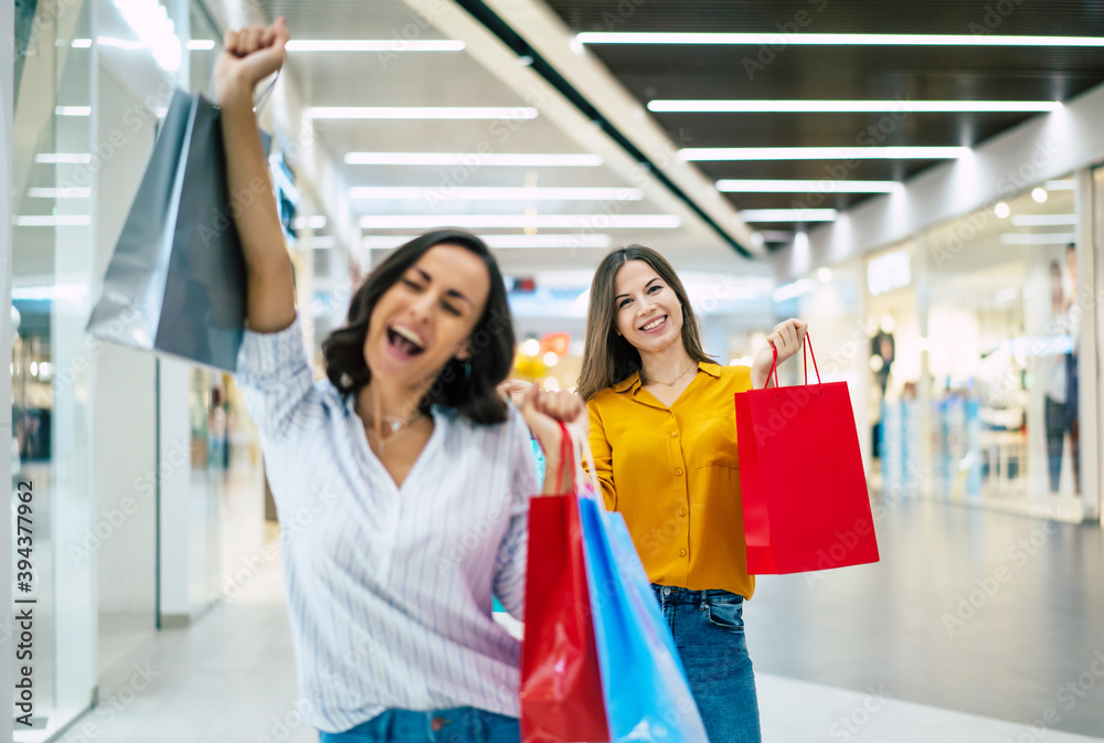 Beautiful happy and excited young girl friends with paper bags are walking around the shopping mall Beautiful happy and excited young girl friends with paper bags are walking around the shopping mall