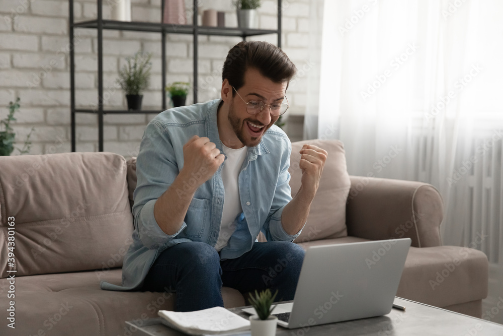 Overjoyed euphoric young man in eyewear looking at laptop screen, reading email with unexpected good news, getting dream job offer, winning prize in online lottery or passed professional exams. Overjoyed euphoric young man in eyewear looking at laptop screen, reading email with unexpected good news, getting dream job offer, winning prize in online lottery or passed professional exams.