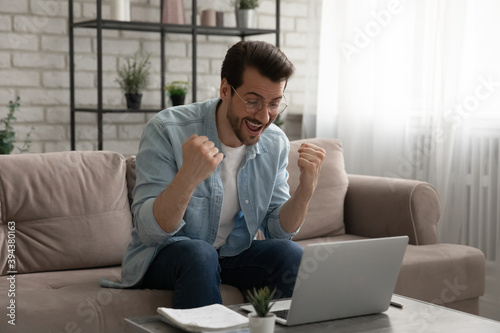 Overjoyed euphoric young man in eyewear looking at laptop screen, reading email with unexpected good news, getting dream job offer, winning prize in online lottery or passed professional exams. © fizkes