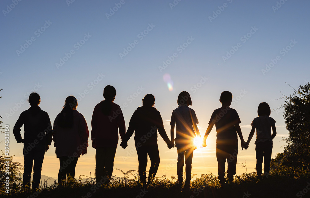 Silhouette of group children standing on mountain at sunset