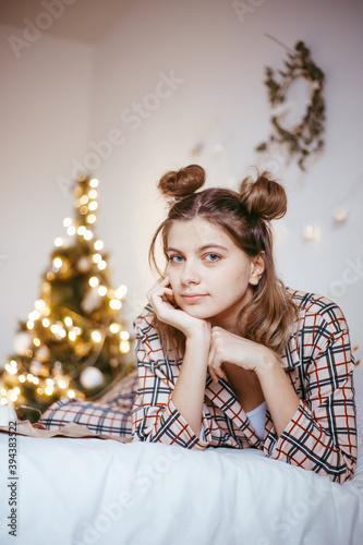 Happy young adult woman wake up at morning in cozy bedroom with decorated christmas tree, raised hands up, making smiling face