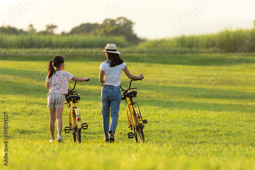Mother and daughter with bicycling at the garden meadow in sunset near white fence. Lifestyle Family Concept