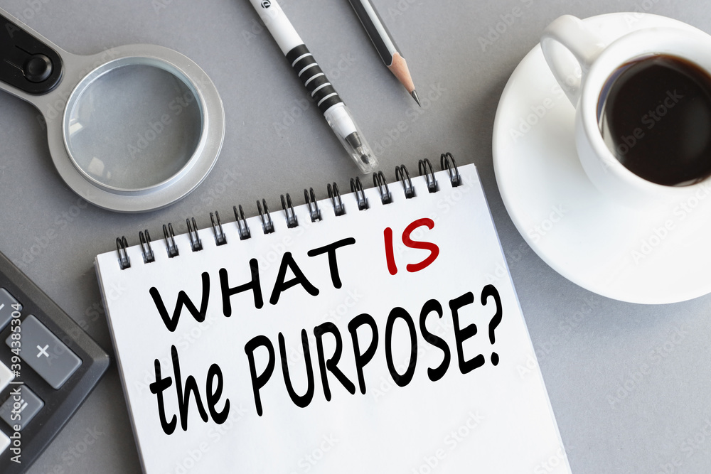 WHAT IS THE PURPOSE ?. text on white paper on gray background near coffee cup and magnifier. WHAT IS THE PURPOSE ?. text on white paper on gray background near coffee cup and magnifier.