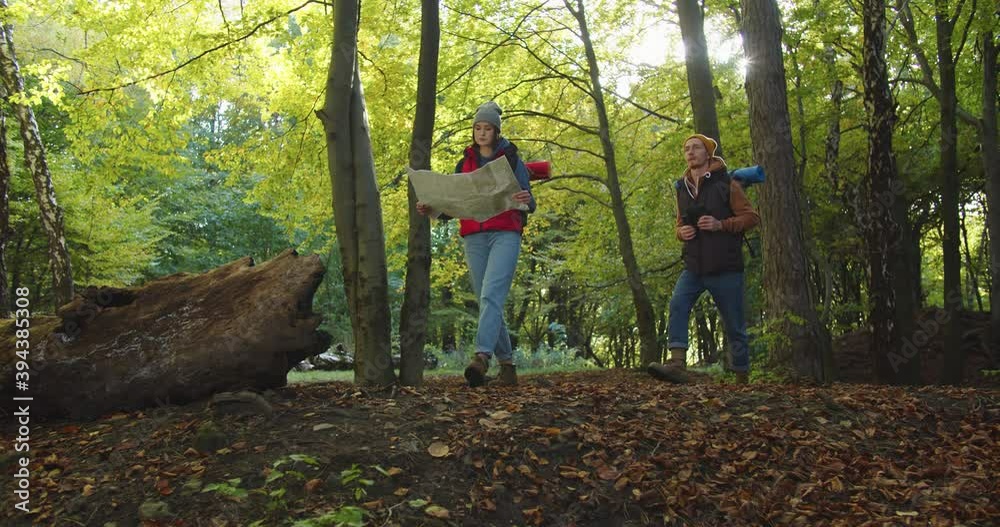 Loving couple handsome man and woman walking in the woods. Woman examines looking at map, man looking through binoculars to find way. Concept of people traveling in nature. Hiker Journey in Wildlife Loving couple handsome man and woman walking in the woods. Woman examines looking at map, man looking through binoculars to find way. Concept of people traveling in nature. Hiker Journey in Wildlife