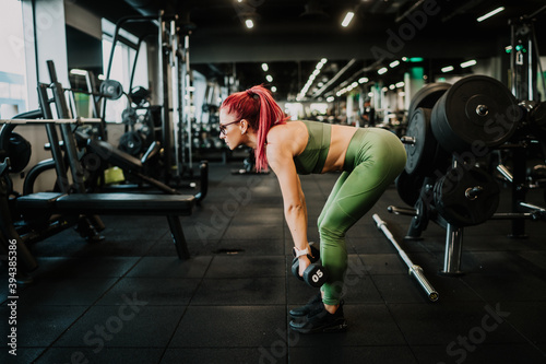Active woman working out at gym. Arms training with barbell and dumbbells.