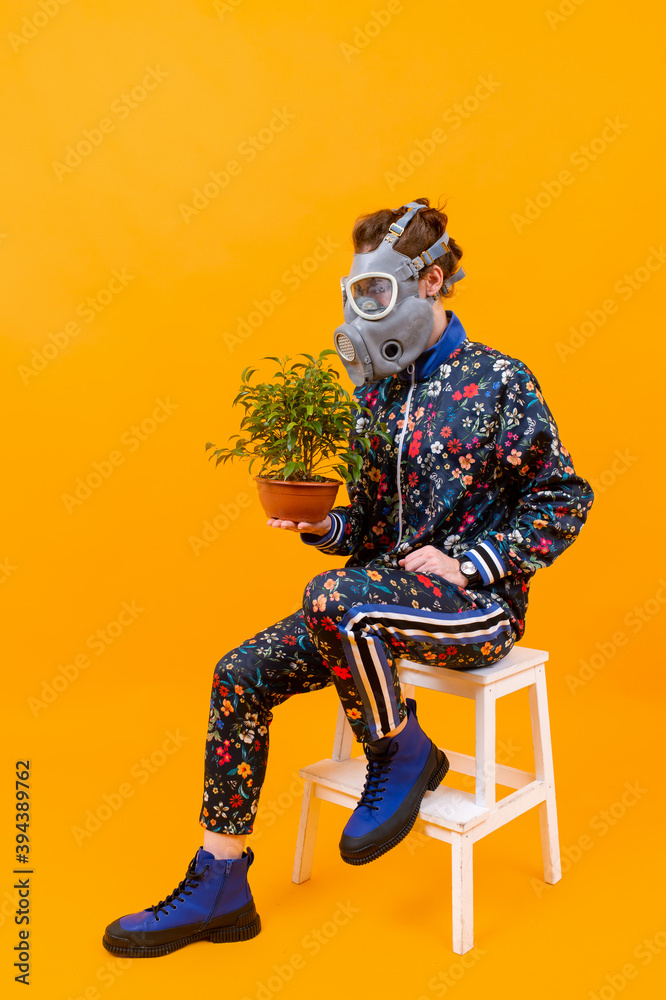 Stylish strange woman in respirator sitting on stepladder with flower in the pot over orange background Stylish strange woman in respirator sitting on stepladder with flower in the pot over orange background