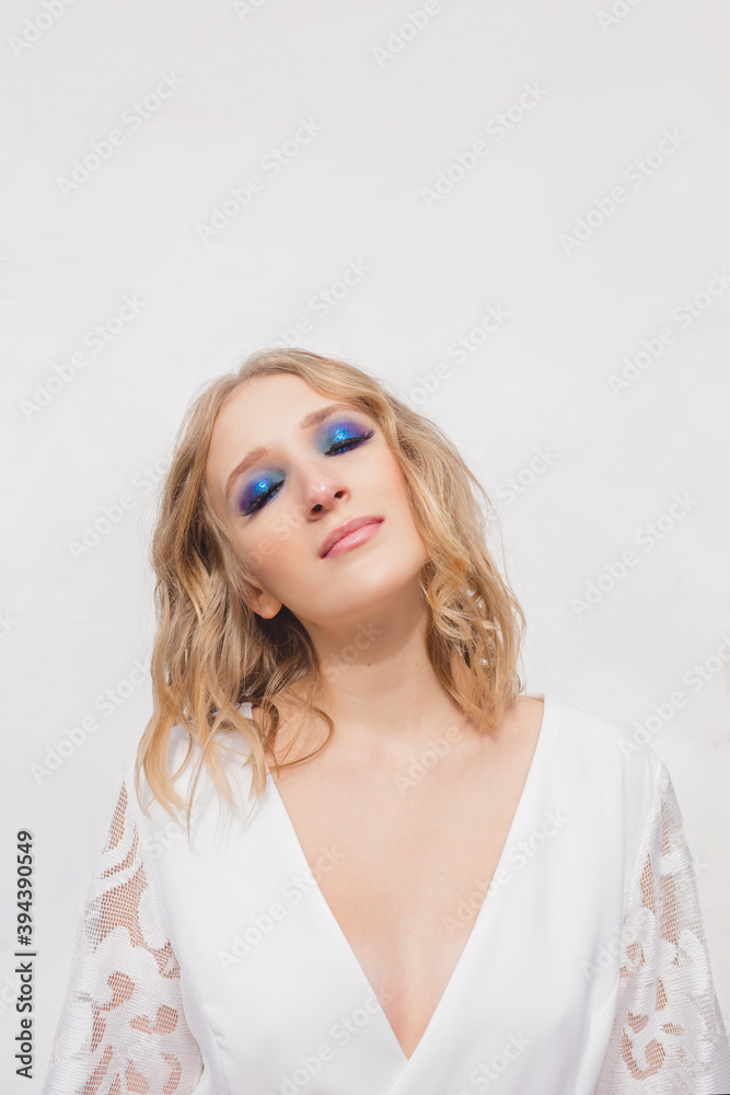 Pretty young stylish blonde with blue eye shadow in white dress. Make up, fashion, magic, style, holidays, miracle concept Pretty young stylish blonde with blue eye shadow in white dress. Make up, fashion, magic, style, holidays, miracle concept