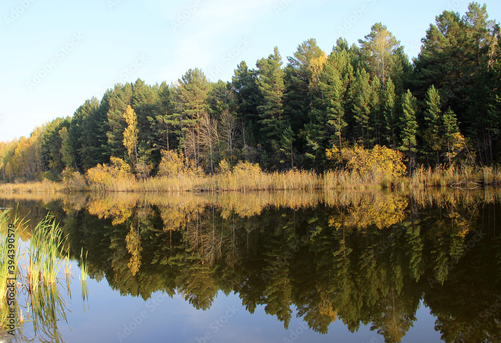 In the still surface of the water of the amazing lake, trees and the sky are reflected as in a mirror.