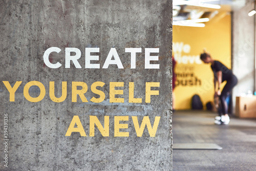 Fitness motivation quote Create Yourself Anew written on grey beton wall at gym, people working out on the background photo