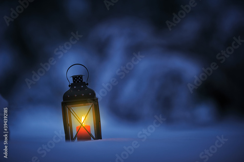 Candle lantern in snow against defocused bokeh background