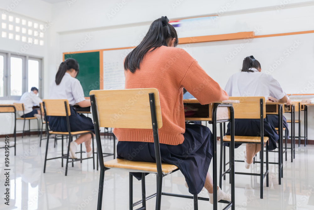 Writing test in exam with behind girl Asian students group concentrate in high school, serious taking final examination desk at classroom with Thai student uniform. Education evaluation concept Writing test in exam with behind girl Asian students group concentrate in high school, serious taking final examination desk at classroom with Thai student uniform. Education evaluation concept