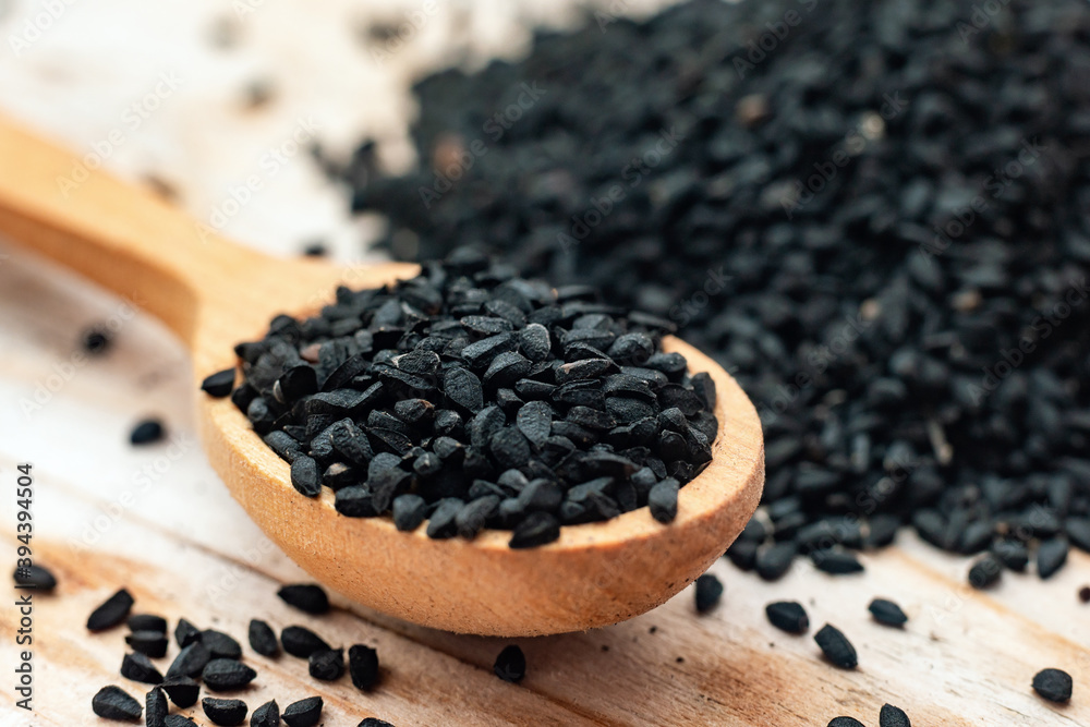 Black cumin seeds on wooden spoon on wooden background Black cumin seeds on wooden spoon on wooden background