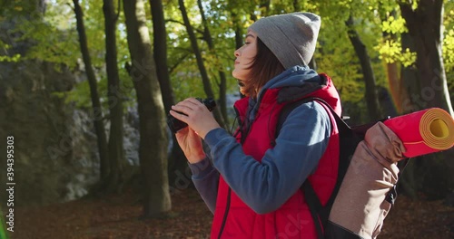 Close up of young woman standing in forest. Female tourist looking thruogh binoculars on background of woods landscape. Concept of people traveling in nature. Hiker Journey in Wildlife photo