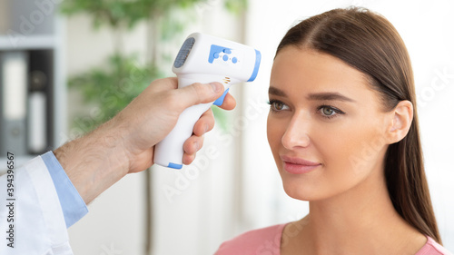 Doctor checking temperature of female patient using infrared thermometer