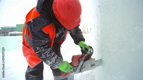 Workman assembler in a protective helmet with a chainsaw in his hands cuts the ice block